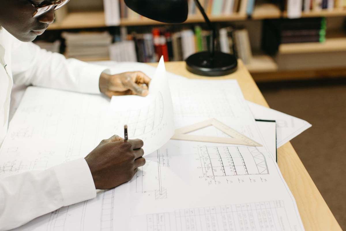 Architect drafting over 2D technical drawings with a set square at his desk