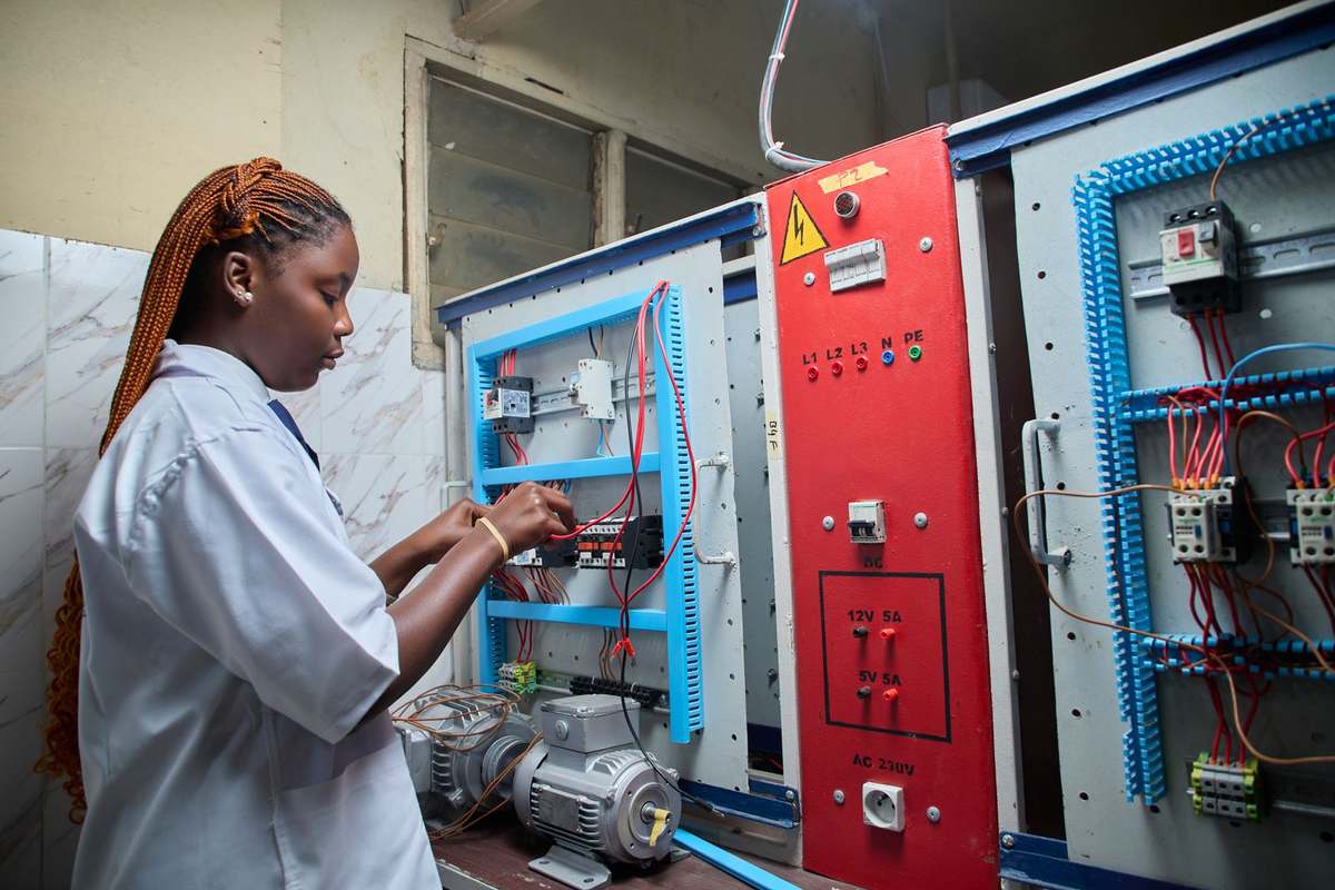 Female technician in a lab coat wiring an electrical control training panel
