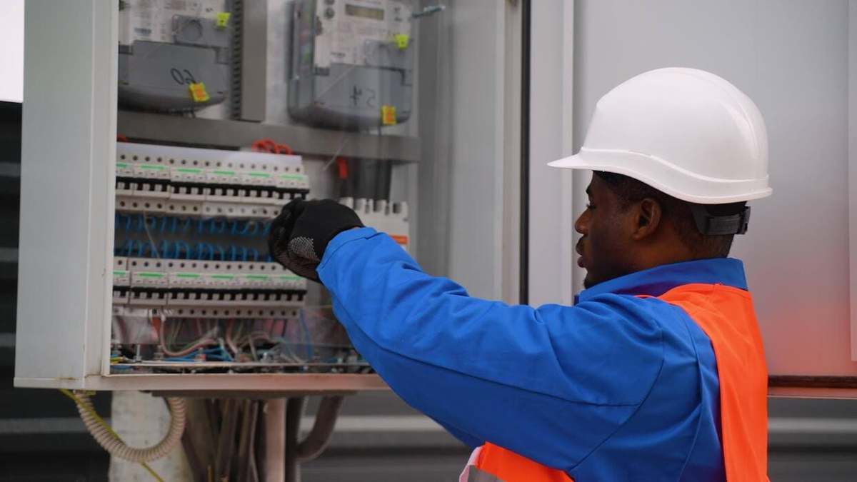 Electrician in a white hard hat and hi-vis vest working on the circuit breakers of an electrical distribution board
