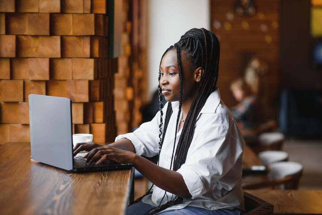 Femme aux longues tresses tapant sur un ordinateur portable à une table de café en bois