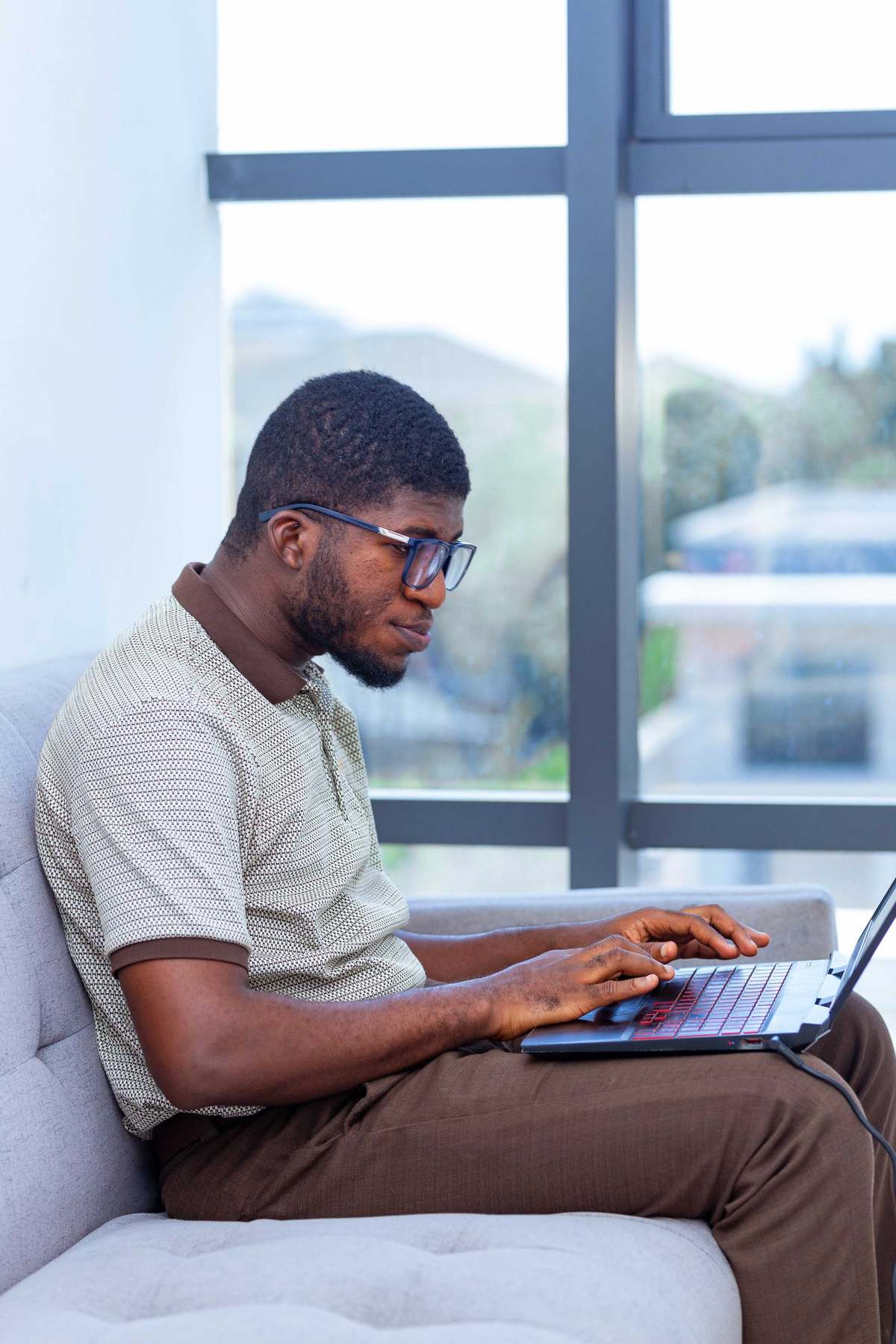Man in glasses typing on a laptop by a bright window in Accra