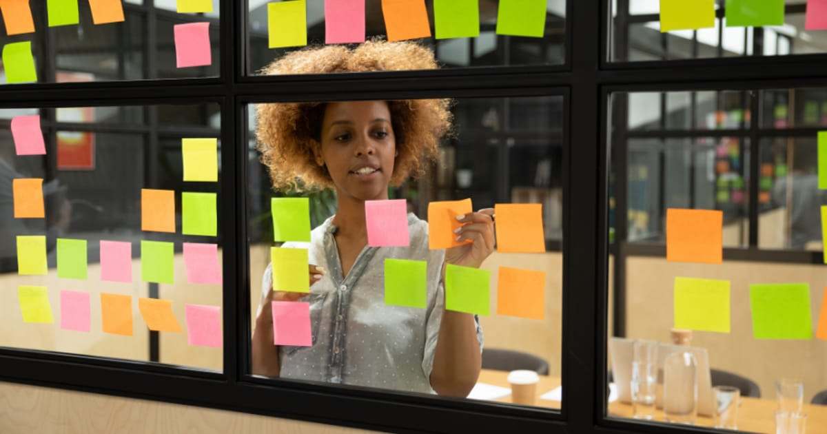 Femme disposant des notes adhésives colorées sur une paroi vitrée de bureau pour planifier un projet