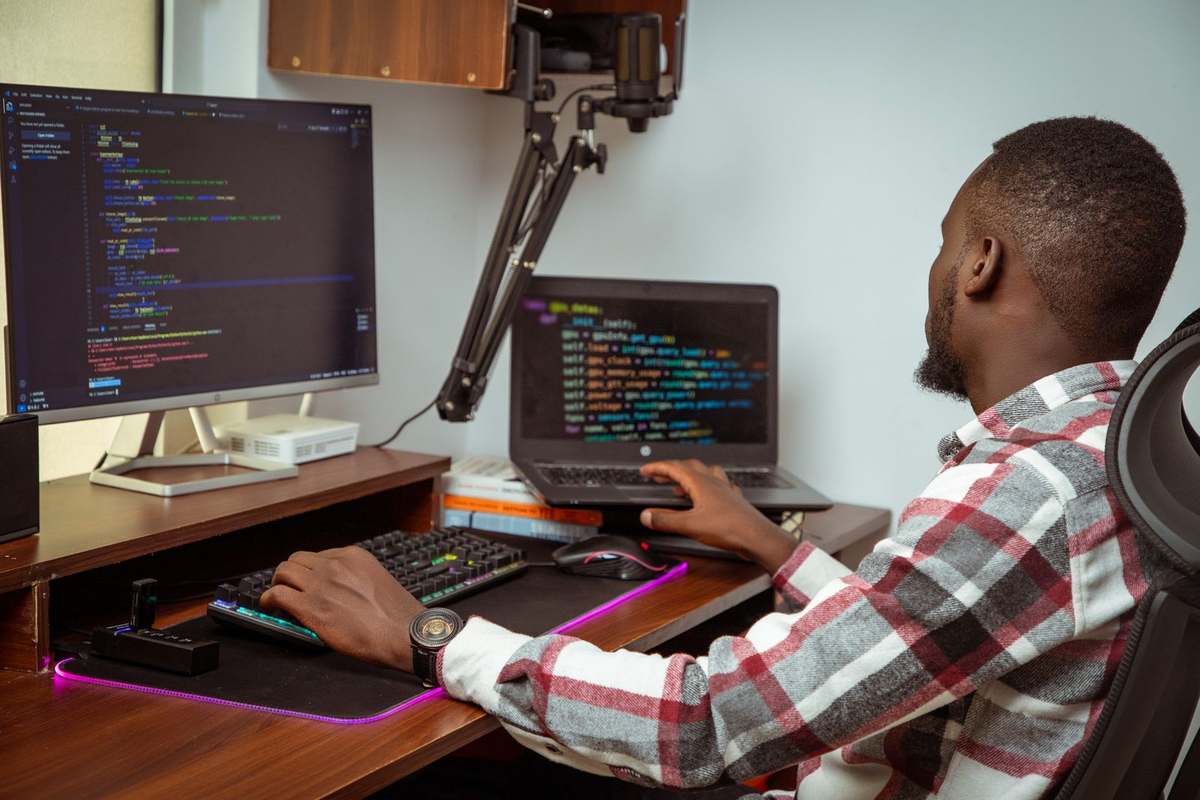 African developer coding across two screens at a modern office workstation