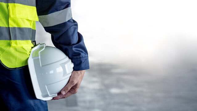 Travailleur en veste bleu marine et gilet haute visibilité tenant un casque de sécurité blanc