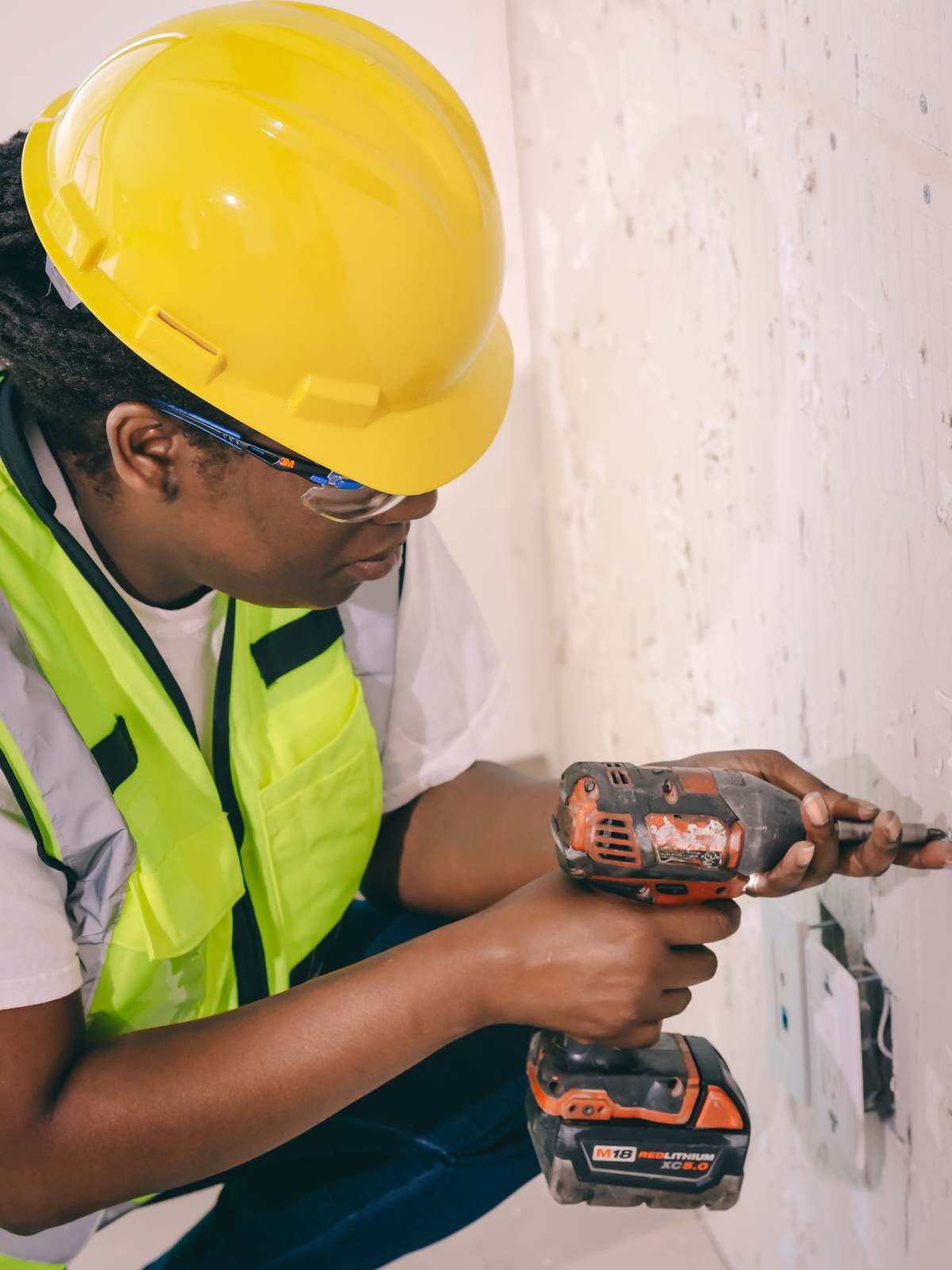 Worker in hard hat, safety glasses and hi-vis vest using a power drill