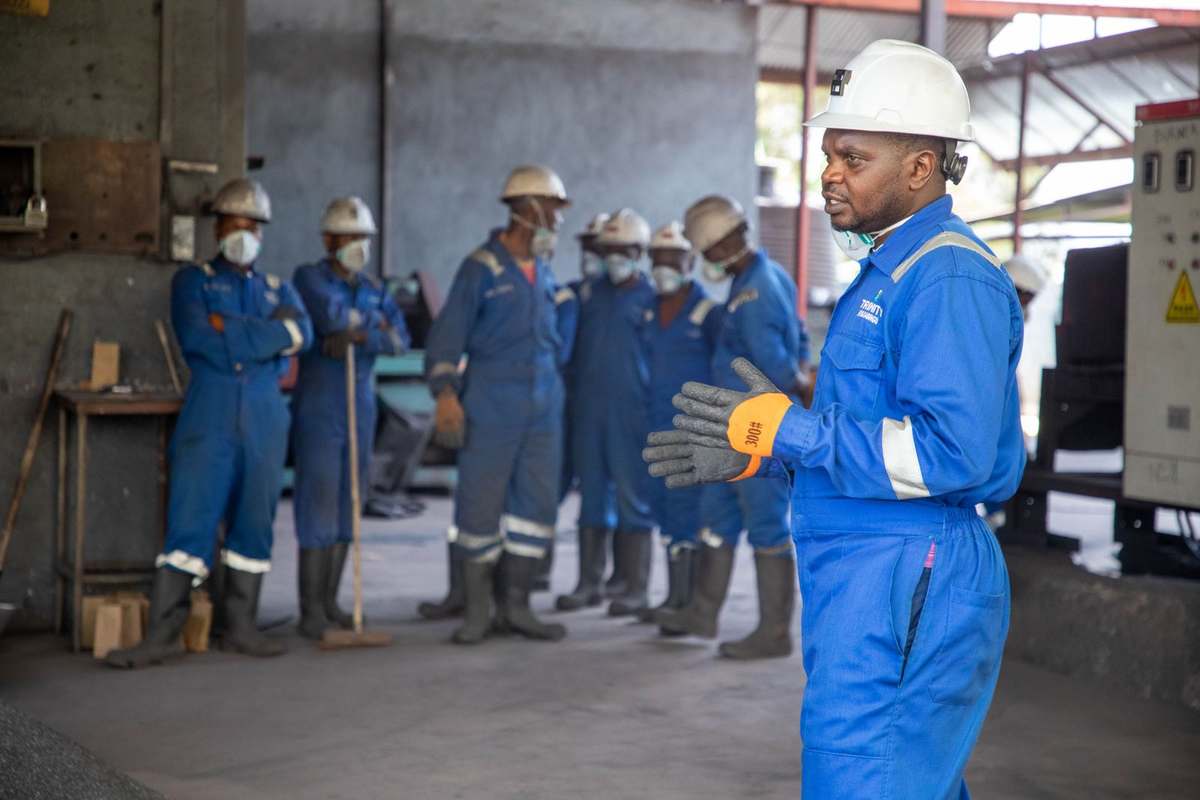 African instructor in coveralls and hard hat leading a safety briefing for trainees in a technical workshop